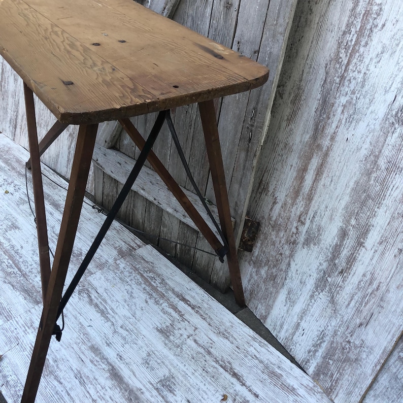 K&ouml;nnte beinhalten: Ein klappbarer Holztisch mit schlichtem Design. Der Tisch hat eine rechteckige Tischplatte und vier Beine, die zum einfachen Verstauen zusammengeklappt werden k&ouml;nnen. Der Tisch ist aus Naturholz gefertigt und hat einen rustikalen Look.