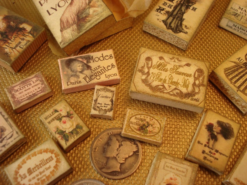 Peut inclure: Une collection de bo&icirc;tes de style vintage avec diff&eacute;rents motifs et textes. Les bo&icirc;tes sont en carton et ont un aspect vieilli. Le texte sur les bo&icirc;tes comprend "Modes Aux Elegantes", "Mlles Sauveur", "Cartier", et "An Merbeilleux".