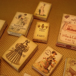 Peut inclure: Une collection de bo&icirc;tes de parfum parisiennes vintage avec des illustrations de femmes dans diff&eacute;rentes poses. Les bo&icirc;tes sont en carton et ont un fond cr&egrave;me avec des lettres dor&eacute;es. Le texte sur les bo&icirc;tes comprend "Maison", "Worth", "Paris", "Corset Persephone", "Mlle Milletrie", "24 Rue du Calvaire", "Au Bon March&eacute;", et "de Paris".