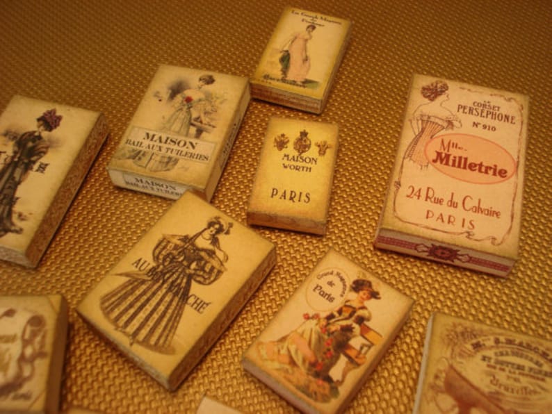 Peut inclure: Une collection de bo&icirc;tes de parfum parisiennes vintage avec des illustrations de femmes dans diff&eacute;rentes poses. Les bo&icirc;tes sont en carton et ont un fond cr&egrave;me avec des lettres dor&eacute;es. Le texte sur les bo&icirc;tes comprend "Maison", "Worth", "Paris", "Corset Persephone", "Mlle Milletrie", "24 Rue du Calvaire", "Au Bon March&eacute;", et "de Paris".