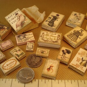 Peut inclure: Une collection de bo&icirc;tes miniatures avec des motifs et des textes vintage. Les bo&icirc;tes sont d&eacute;cor&eacute;es d'images de femmes en robes, de fleurs et d'autres &eacute;l&eacute;ments d&eacute;coratifs. Les bo&icirc;tes sont en carton et ont un aspect vieilli. Le texte sur les bo&icirc;tes comprend les mots "Paris", "Modes", "Elegantes" et "Au Merveilleux".