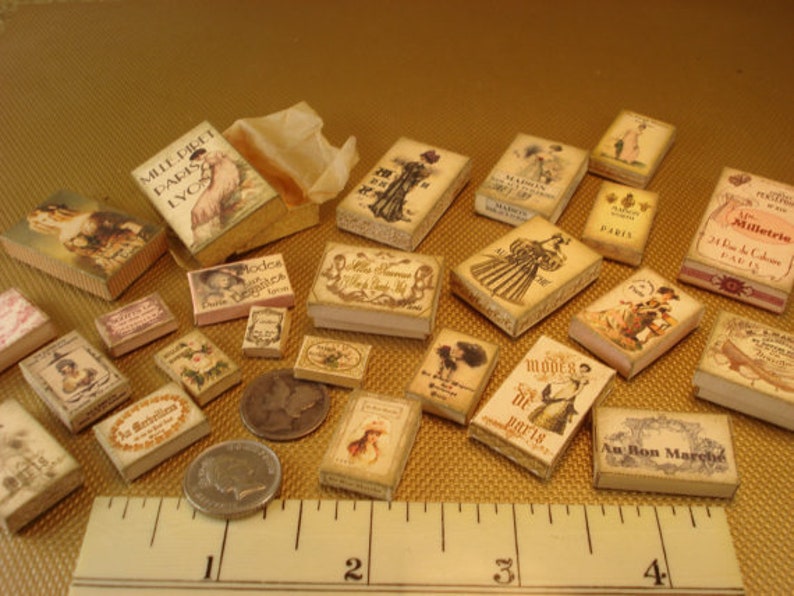 Peut inclure: Une collection de bo&icirc;tes miniatures avec diff&eacute;rents motifs et textes, dont "Mille Dilet Paris LVO", "Modes", "Paris", "Milletria 24 Rue de la Colombe Paris", et "Au Bon March&eacute;".