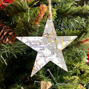 May include: A white star-shaped Christmas ornament with a map of Chorlton, Manchester, England printed on it. The ornament is hanging on a Christmas tree.