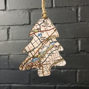 May include: A wooden Christmas tree decoration shaped like a map of a small town. The ornament features a map with roads, buildings, and a small lake. The text on the map includes "Lower High Trees", "Wood End", "Branch Road", "Stubbing Wood", and "Beestonley".