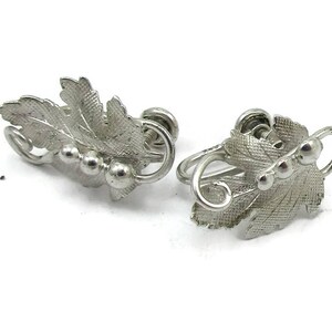 May include: A pair of silver tone clip-on earrings featuring a leaf design with small round accents.
