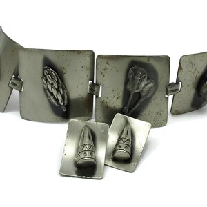 May include: A silver bracelet with five square links, each featuring a different embossed design. The bracelet is accompanied by two matching earrings with similar designs.