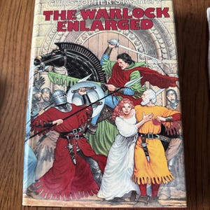May include: A book titled The Warlock Enlarged by Christopher Stasheff featuring a fantasy illustration on the cover. The artwork depicts a knight on a black horse, a warrior in red robes with a sword, a woman in a white dress, and a man in yellow.