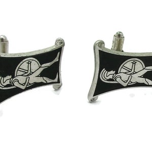 May include: A pair of silver cufflinks with a black enamel background. Each cufflink features a stylized image of a person lying down with a wheel.