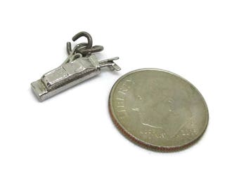 May include: Silver charm depicting a golf bag with clubs and a golf ball. The charm is about the size of a US dime.