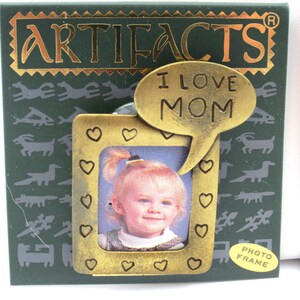 May include: A gold-toned photo frame with a heart-shaped border and a speech bubble that says "I Love Mom". The frame is on a green background with a pattern of stylized animals. The frame is labeled "Photo Frame".
