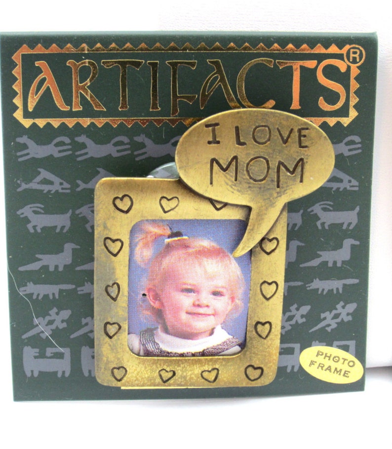 May include: A gold-toned photo frame with a heart-shaped border and a speech bubble that says "I Love Mom". The frame is on a green background with a pattern of stylized animals. The frame is labeled "Photo Frame".