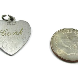 May include: Silver heart-shaped charm with the inscription "Conk" and the words "Sterling Automade" on the back. The charm is next to a US dime for size comparison.