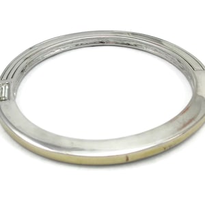 Puede incluir: Un brazalete de plata con una banda dorada y una sola piedra transparente engastada en el metal.
