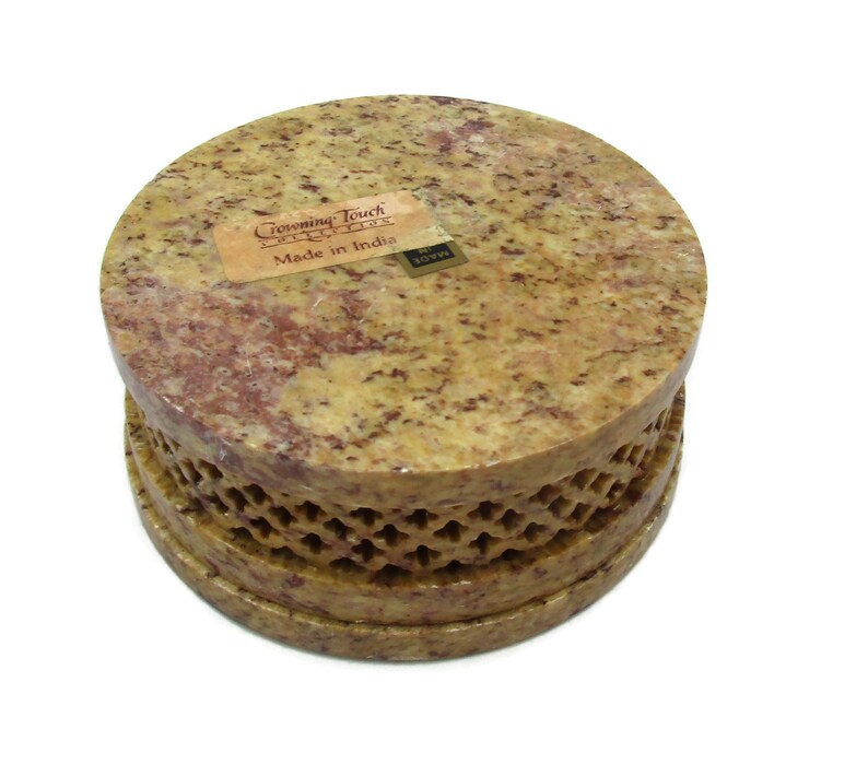 May include: A round, yellow and brown stone box with a carved design around the bottom edge. The box has a label that reads "Crowning Touch Imports" and "Made in India".