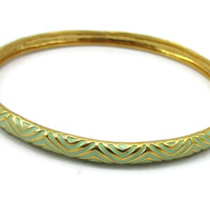 Op de afbeelding: Een gouden armband met een groen chevron-patroon.
