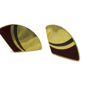 May include: A pair of gold-tone earrings with a geometric design. The earrings are shaped like a crescent moon and have a black and burgundy enamel design.