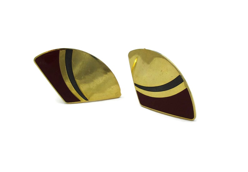 May include: A pair of gold-tone earrings with a geometric design. The earrings are shaped like a crescent moon and have a black and burgundy enamel design.