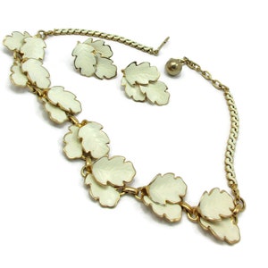 May include: A gold chain necklace with white enamel leaf charms and matching earrings. The necklace has a lobster clasp closure.