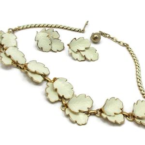 May include: A white enamel leaf necklace and earrings set. The necklace features a chain with multiple white enamel leaves attached. The earrings are a pair of white enamel leaves.