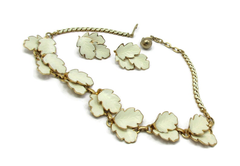May include: A white enamel leaf necklace and earrings set. The necklace features a chain with multiple white enamel leaves attached. The earrings are a pair of white enamel leaves.