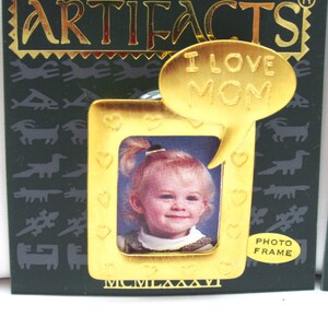May include: Gold-toned photo frame with a heart design and a speech bubble that says "I love Mom". The frame is on a green background with a pattern of stylized animals.