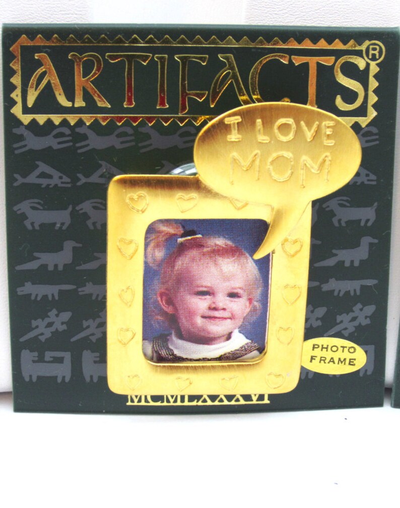 May include: Gold-toned photo frame with a heart design and a speech bubble that says "I love Mom". The frame is on a green background with a pattern of stylized animals.