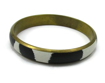 May include: A gold bangle bracelet with black and white stripes.