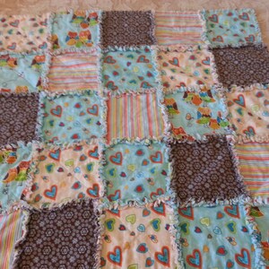 May include: A patchwork quilt with a variety of colorful fabrics featuring owls, hearts, and floral patterns. The quilt is made with a scrappy style and has a frayed edge.