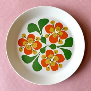 May include: A white ceramic plate with a floral design. The flowers are orange, yellow, and green.
