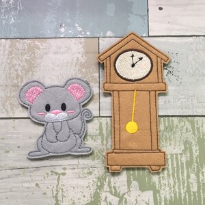 May include: A gray felt mouse with pink ears and a white nose sits next to a brown felt grandfather clock with a yellow pendulum.