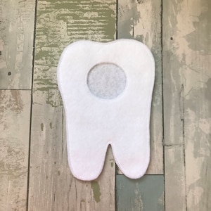May include: White felt tooth shape with a hole in the center. The tooth is a craft supply for a children's project.