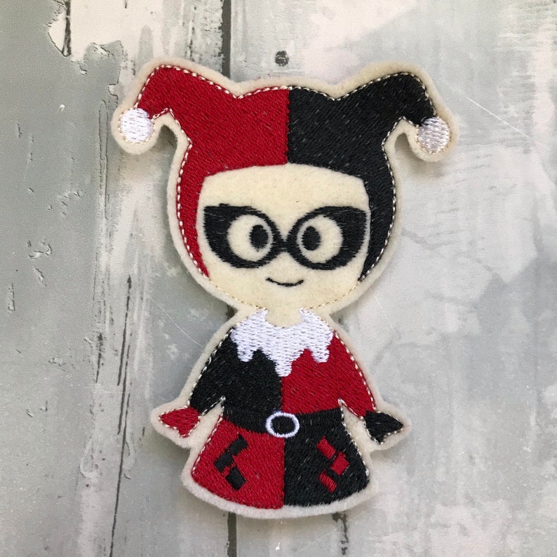 May include: Embroidered felt patch of a cartoon character with red and black jester's hat, black and red costume, and black glasses.