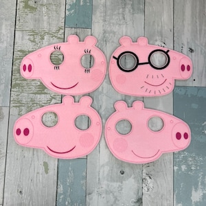 May include: Four pink felt pig masks with black embroidered features. Two masks have eyes and a smile, one has glasses and a moustache, and one has just eyes.