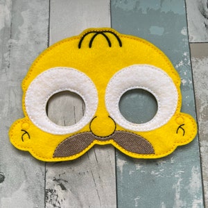 Puede incluir: M&aacute;scara de fieltro amarilla con pelo negro, ojos blancos y bigote marr&oacute;n. La m&aacute;scara est&aacute; dise&ntilde;ada para parecerse a un personaje de dibujos animados.