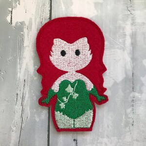 May include: Embroidered felt patch of a cartoon character with red hair, a green leafy costume, and a white face.