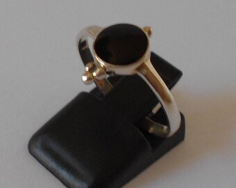 May include: A silver ring with a black onyx stone set in a bezel setting. The ring has a simple design and is accented with small gold accents.
