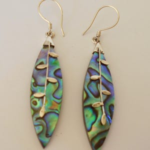 May include: A pair of silver earrings with a green, blue, and iridescent abalone shell design. The earrings feature a silver stem with small silver leaves.