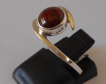May include: A silver ring with a red gemstone set in a bezel setting. The ring is marked "925" on the side.
