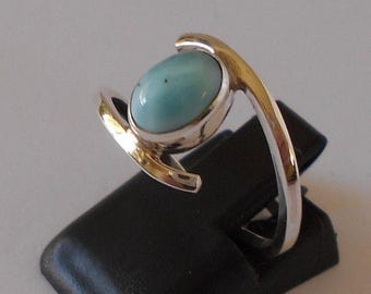 May include: A silver ring featuring a light blue oval gemstone. The ring has a unique, curved design with a polished finish. The gemstone is set in a silver bezel.