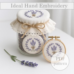 May include: A glass jar with a white fabric lid, featuring a lavender embroidery design, is next to a matching embroidered patch and a wooden embroidery hoop. A sprig of lavender and the text "Ideal Hand Embroidery" are also visible.