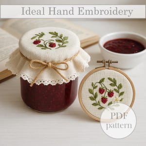 Könnte beinhalten: Ein Glas mit roter Marmelade, bedeckt mit einem Stoffdeckel mit gestickten grünen Blättern und roten Beeren. Ein Stickrahmen mit ähnlichem Design daneben. Der Text "Ideal Hand Embroidery" steht oben.
