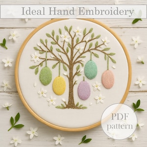 May include: Embroidered hoop art featuring a tree with green leaves and white flowers, with five colorful eggs hanging from the branches. The hoop is on a white wooden background with white flowers scattered around it. The text "PDF pattern" is in the lower right corner.