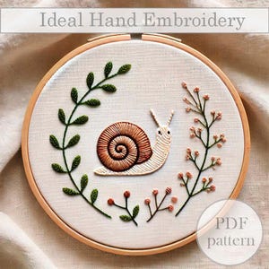 May include: A hand embroidery pattern featuring a snail with a brown shell and green and pink floral accents. The pattern is displayed on a wooden embroidery hoop. The text "PDF pattern" is visible in the lower right corner of the image.