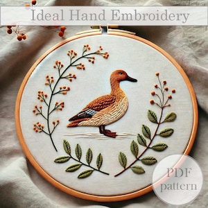 May include: A hand embroidery pattern featuring a brown and white duck with orange accents, surrounded by green and orange leaves. The pattern is printed on a white background and includes the text "PDF pattern".