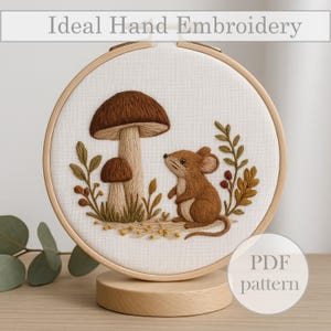 Peut inclure: Broderie à la main dans un cercle en bois, représentant un champignon brun, une souris et des feuilles. Le texte "Ideal Hand Embroidery" est en haut. Un patron PDF est disponible.