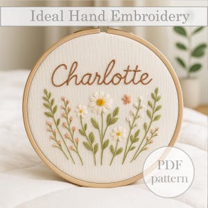 Può includere: Ricamo a mano su telaio con il nome "Charlotte" in filo marrone. Il design include margherite ricamate, piccoli fiori e foglie verdi. È visibile anche il testo "Ideal Hand Embroidery" e "PDF pattern".