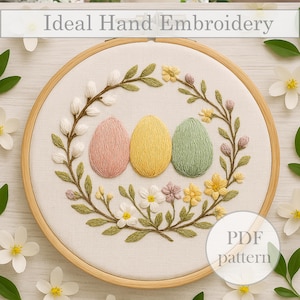 May include: Embroidery hoop with a floral wreath design featuring three pastel colored eggs. The wreath is made of green leaves and white flowers. The text "PDF pattern" is visible in the lower right corner.