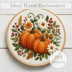 May include: Hand-embroidered fall-themed hoop art featuring two orange pumpkins, white daisies, and autumn foliage. The design is set against a cream-colored fabric within a wooden embroidery hoop. The text "Ideal Hand Embroidery" is at the top.