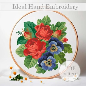 May include: A PDF pattern for hand embroidery featuring a bouquet of red roses and blue pansies with green leaves. The pattern is displayed in a wooden embroidery hoop.