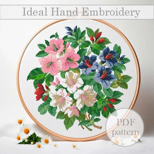 Könnte beinhalten: Ein runder Stickrahmen mit einem Blumendesign mit rosa, weißen und blauen Blumen. Die Blumen sind von grünen Blättern und Stielen umgeben. Der Text "PDF pattern" ist in der unteren rechten Ecke des Rahmens sichtbar.